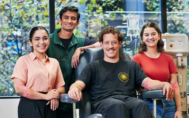 four people in a donor centre smiling at the camera, one is seated in a donor chair
