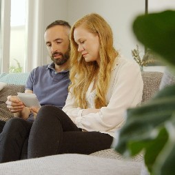 parents sit on sofa looking at item in hands