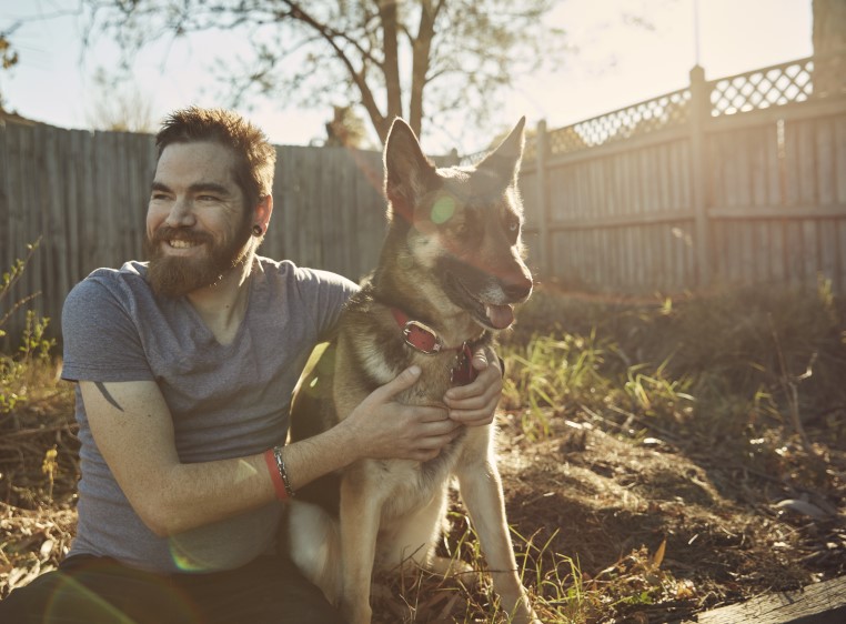 Beau and his dog in a backyard, Beau is looking off camera and smiling