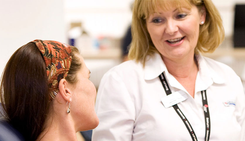 a donor is seated and looking up at a nurse, both are smiling