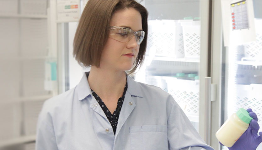 a scientist in front of a fridge holding up a vial of milk