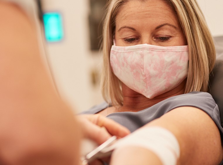 Donor Tess giving blood with a pale pink mask on