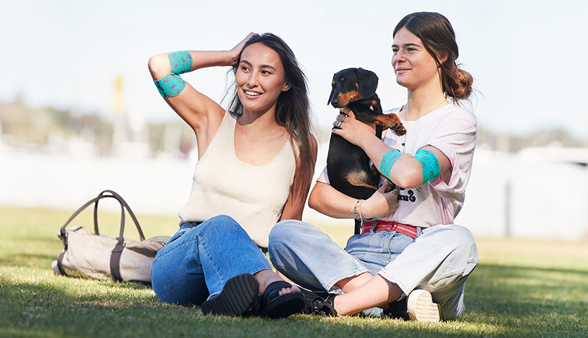 two women are sitting on the grass in a park holding a dog