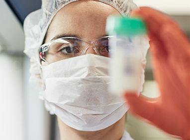 a scientist is wearing a facemask and a hairnet and is holding up a milk sample jar