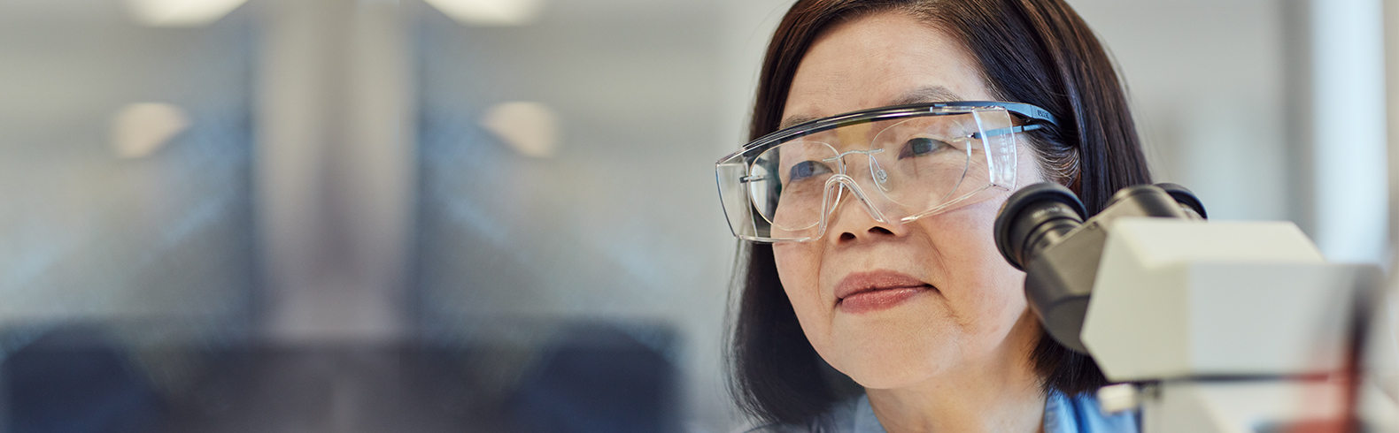 close up of a scientist wearing goggles sitting next to a microscope