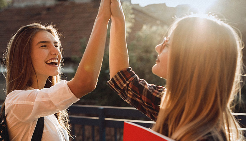  close up photo of two women smiling and high fiving, the sun is shining brightly in the background