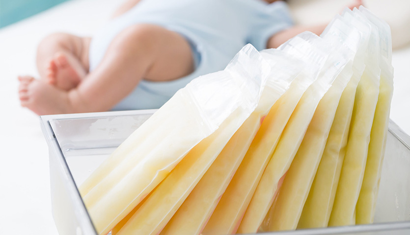 a baby is lying down in the background wearing a blue outfit with several bags of milk in the foreground