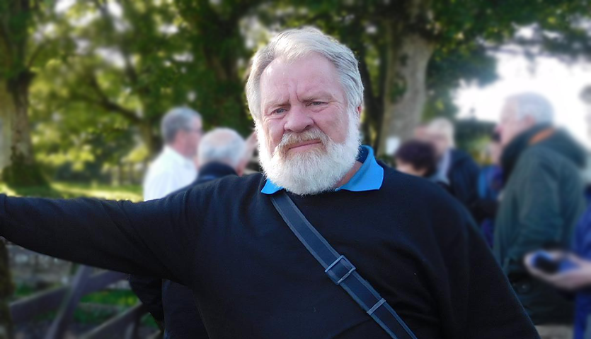 elderly man with a beard facing the camera while leaning on a wall outdoors