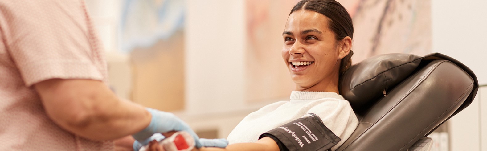 photo of a donor seated in a chair and smiling with a nurse standing in the foreground