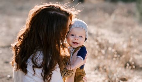 photograph of a woman holding a baby, the baby is wearing a beanie and smiling