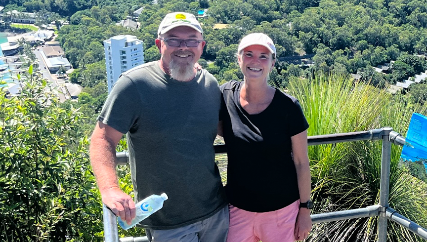 man and woman smiling at the top of a mountain