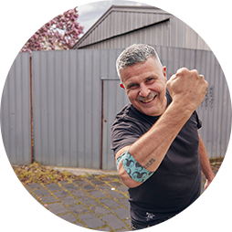 photo of Travis Garone smiling and holding his arm up with the Movember bandage around his elbow