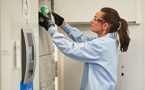 photo of a scientist wearing goggles and placing a box of samples into a freezer