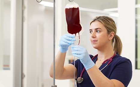 photo of nurse abbey wearing a blue uniform and gloves and holding up a blood bag