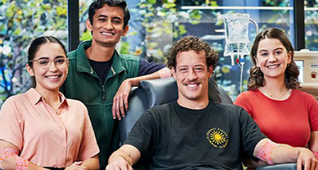a group of people smiling to camera, one is seated in a donor chair