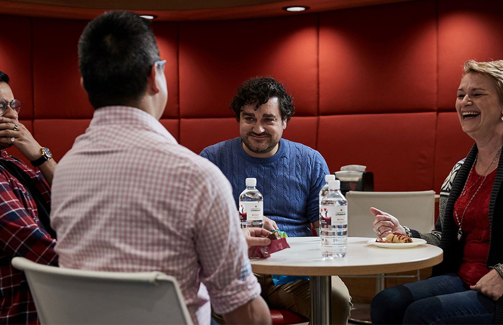 a group of people sitting around a table with snacks and water laughing and chatting