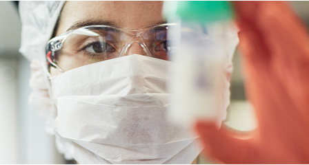 a scientist is wearing a facemask and a hairnet and is holding up a milk sample jar
