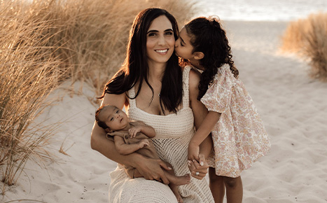 Image of a lady with her infant son and toddler daugher with the ocean in the background