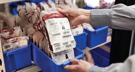 close up of a blood bag being held by person with blood bags in a rack behind