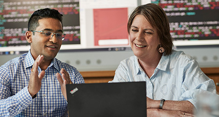 two people seated and talking with a laptop open in front of them