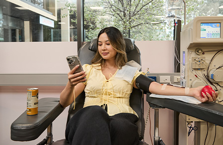 Image of a young female donating blood while looking at her phone