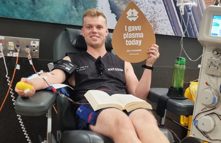 young male plasma donor holding up a sign that says i donated plasma in the donor chair