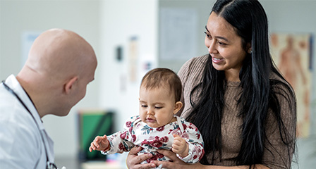 Image of doctor in white coat talking to mother holding a baby