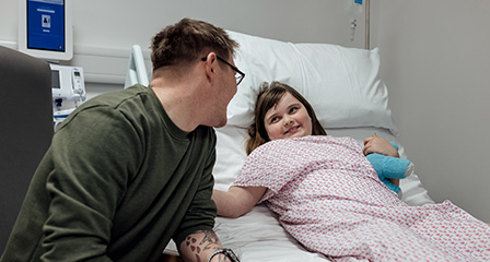 image of a parent sitting next to a child in a hospital bed