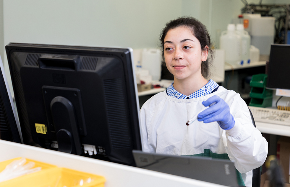 image of scientist holding test tube in front of computer