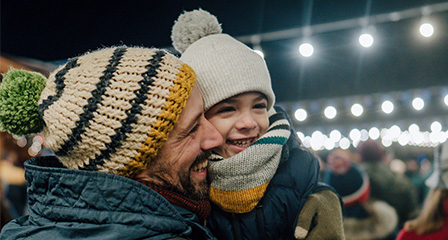 a father and son wearing beanies and smiling with lights in the background