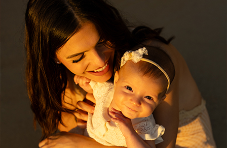 image of a woman holding her baby girl and smiling as the golden sunset shines on their faces