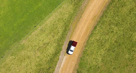 aerial photo of a field with a car driving on a dirt road through it