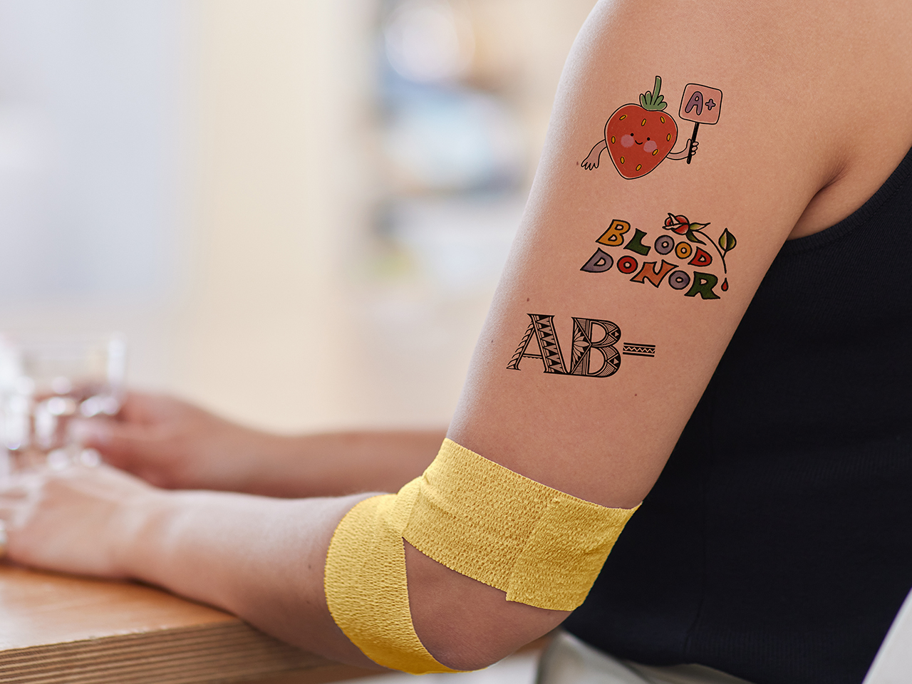closeup of a person's arm with a yellow tattoo around their elbow and three temporary tattoos on their upper arm