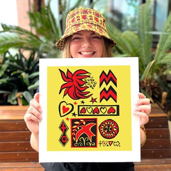 a young woman is smiling and holding up a print of Jenny Kee's design which is yellow with red and black pictures on it, she is wearing a bucket hat with the same print