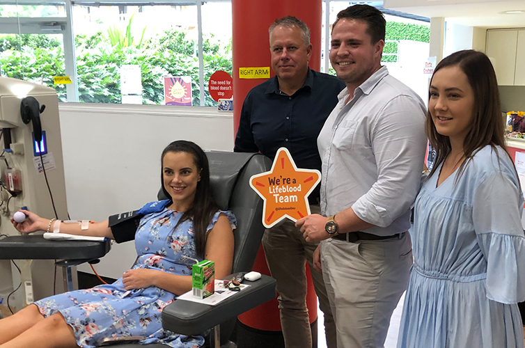 Taylor and colleagues from elders real estate during a donation, one holds a sign in the shape of a star with we're a lifeblood team written on it