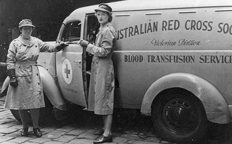 Black and white image of two women standing in front of 1950s van that says "Australian Red Cross Society - Victorian Division - Blood Transfusion Service" 