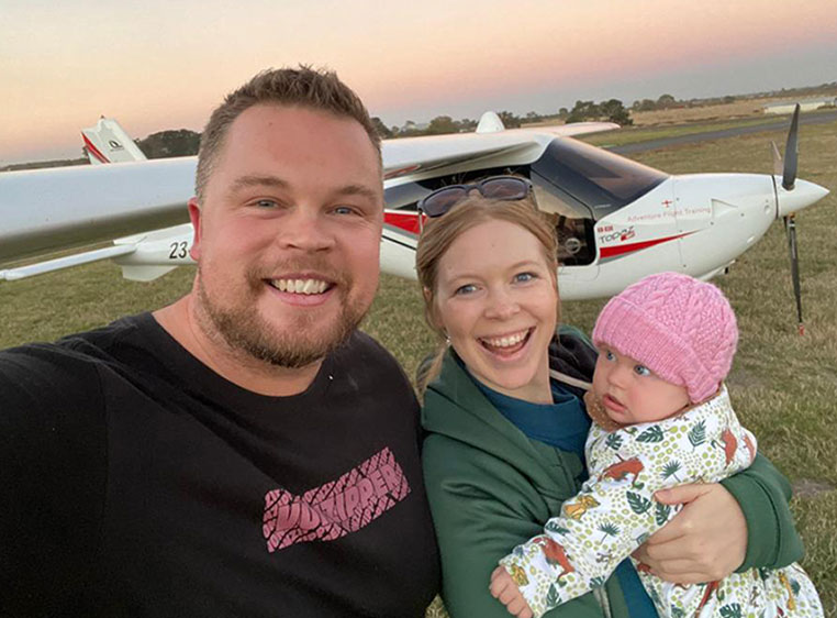 photo of a man and woman with their baby in a field with a sunset behind them