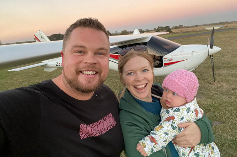 Man and woman smiling outdoors while the woman is holding their baby girl