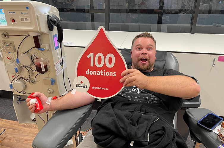 man in the chair donating blood and holding up a sign that says 100 donations