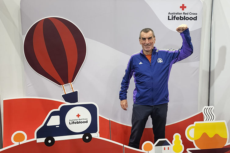 donor Jarrod is smiling in front of a Lifeblood sign holding his left fist in the air