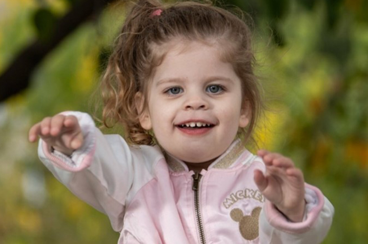 toddler girl smiling at camera wearing a pink jacket outdoors