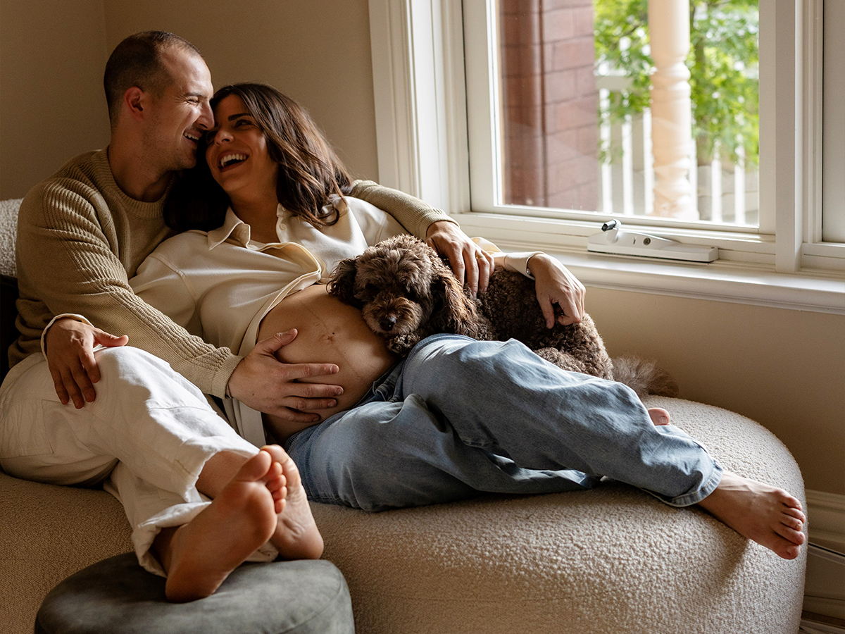 Image of a pregnant woman and her husband with a dog resting on her belly