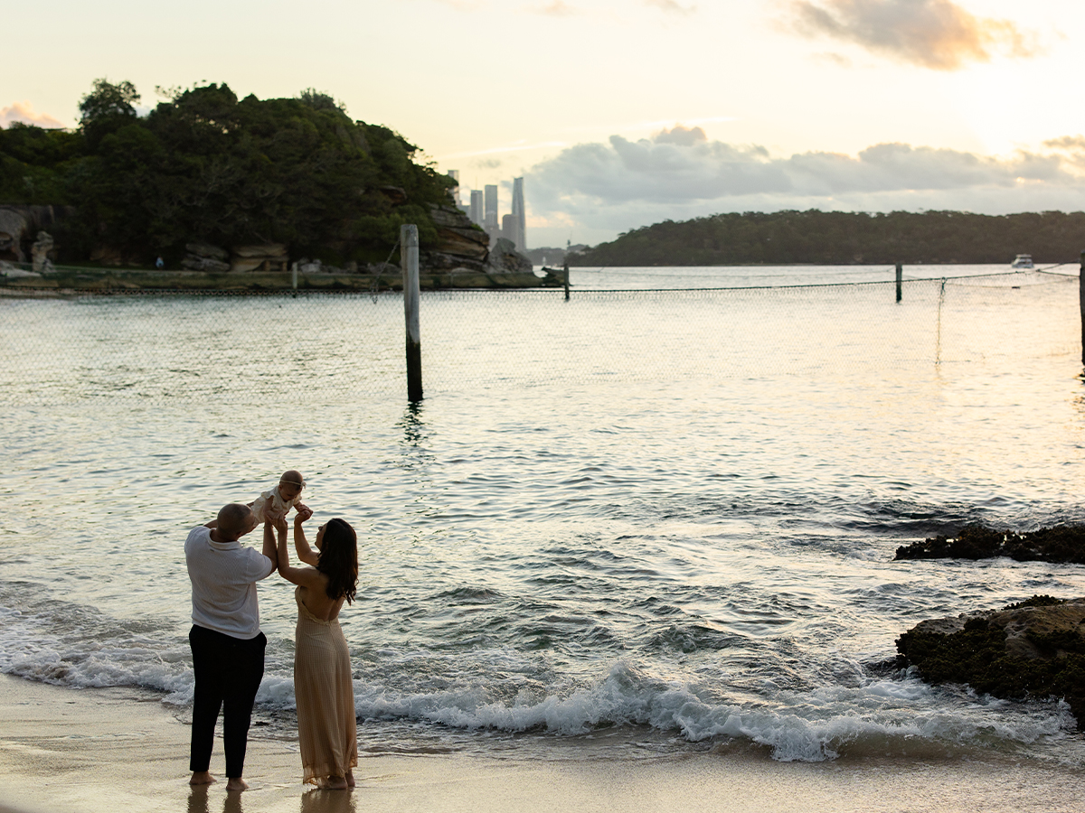 Image of a man and woman holding up their baby girl by the beach side as the sun is setting