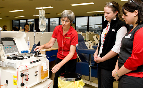 Staff member showing two newer staff members the plasma donation machine in a donation centre