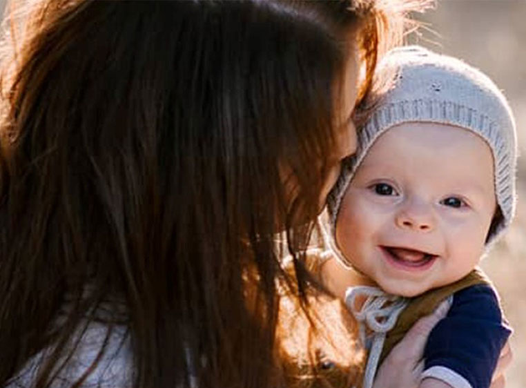 photo of a mother hugging her baby, the baby is wearing a grey knitted beanie and smiling