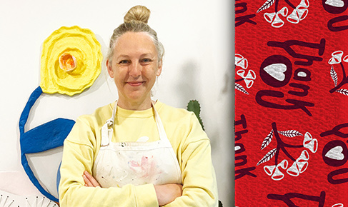 photo of artist Madeleine Stamer wearing an apron and facing the camera with her arms crossed, on the right is her design of the words thank you on a red background and a branch motif