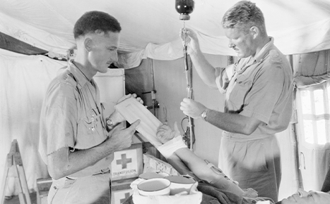 Two male doctors in war-time medical tent working on a patient