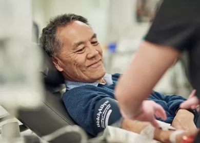 a man sits in a donor chair helped by an assistant with his donation