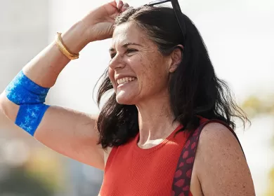 a woman is holding her sunglasses up and smiling off camera, on her elbow is a true colours designed bandage