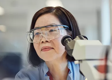 close up of a scientist wearing goggles sitting next to a microscope